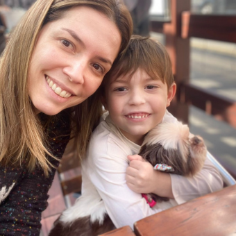 Selfie da Débora ao lado de seu filho que está segurando a Cupcake, uma shih-tzu cega. 