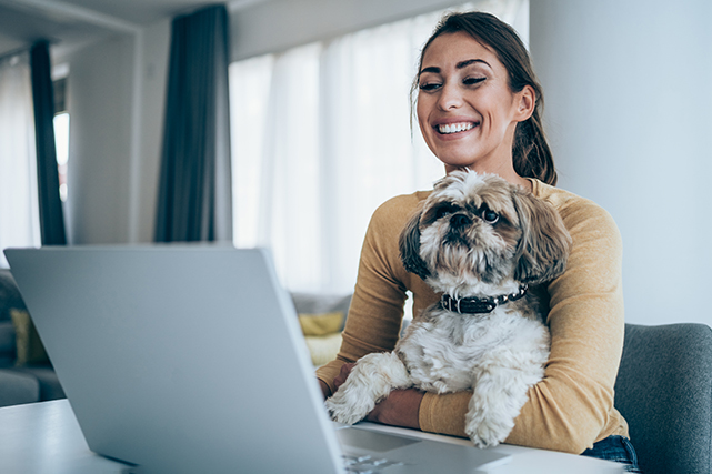 Uma mulher utiliza um notebook, com um cachorro no colo