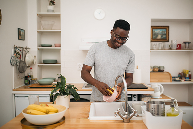 Um homem lava um pote em uma cozinha com decoração branca e marrom.